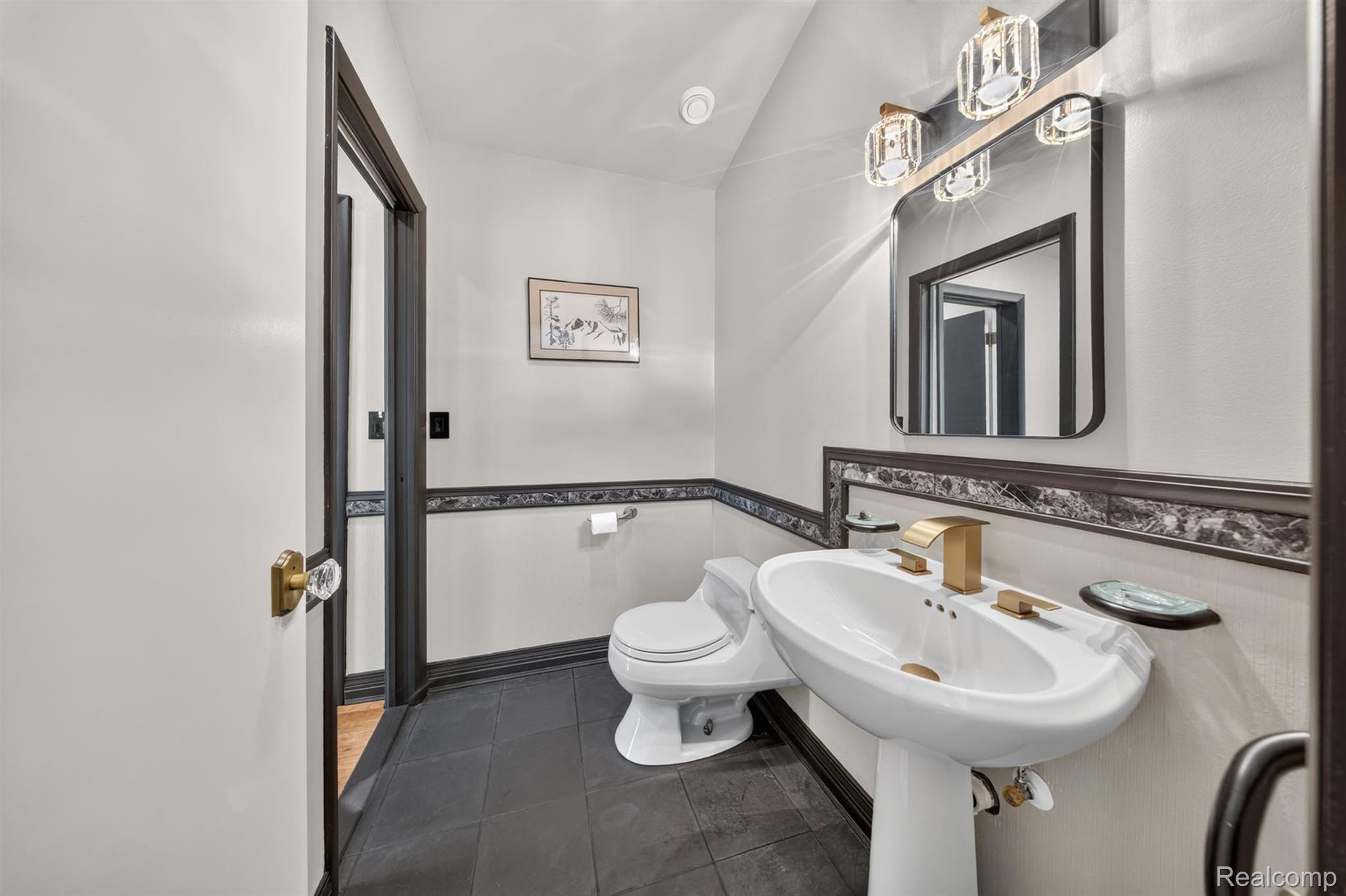 9319 Faussett Road Fenton, MI 48430 - Photo 24 of 70 Pedestal sink with gold-finish faucet, toilet, wall-mounted mirror, and black tile flooring