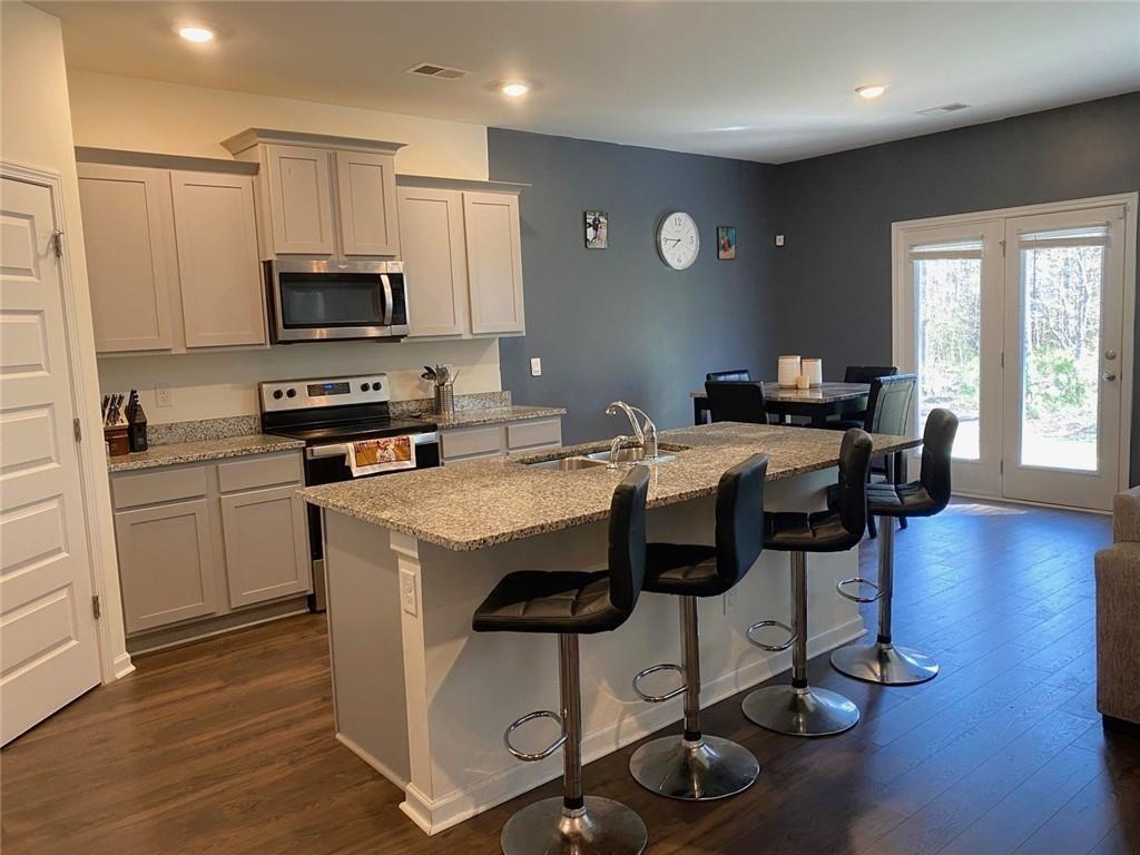 676 Whitman Lane Stockbridge, GA 30281 - Photo 4 of 50 a kitchen with stainless steel appliances a stove a sink a microwave a refrigerator cabinets and a dining table with wooden floor