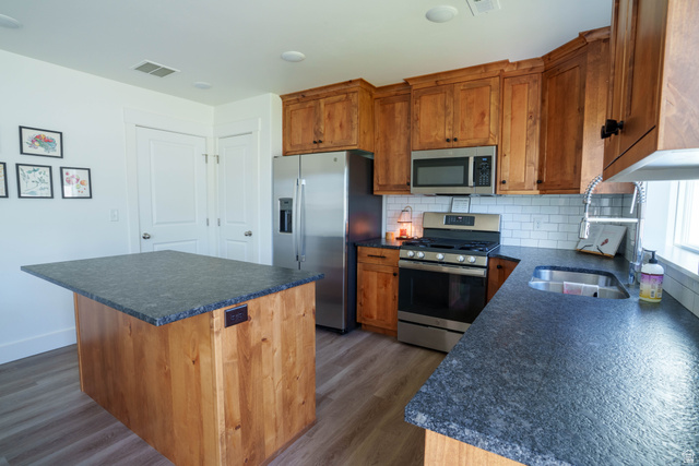 1486 West 2055th Street South Logan, UT 84339 - Photo 11 of 45 Kitchen featuring wood cabinetry, stainless steel appliances, and dark speckled countertops