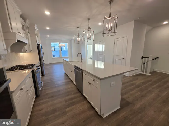 an empty room with wooden floor chandelier fan and kitchen view