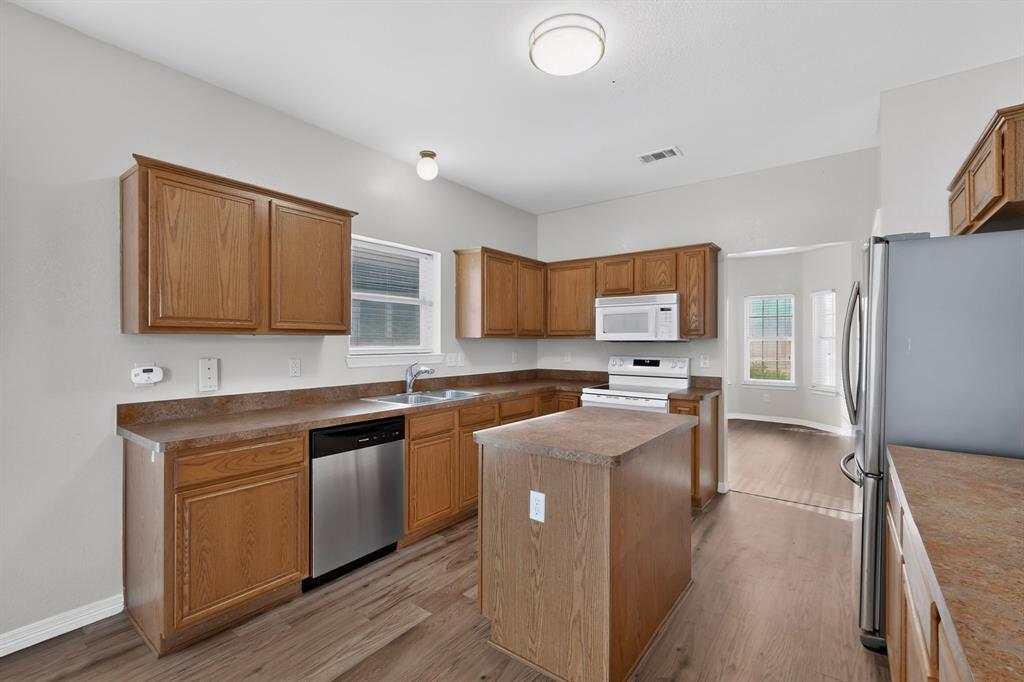 3401 Newgate Street Midlothian, TX 76065 - Photo 13 of 34 Kitchen featuring wood-finish cabinetry, stainless steel dishwasher, white oven and microwave, a central island with countertop, and wood-finish flooring