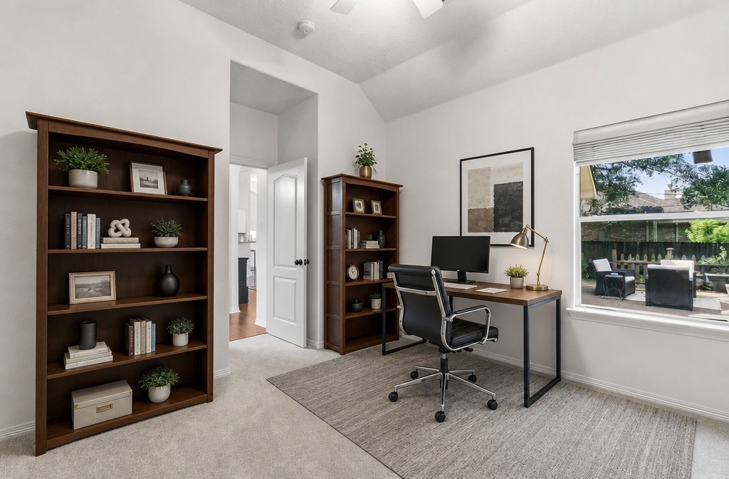 34019 Conroe Huffsmith Road Magnolia, TX 77354 - Photo 6 of 19 A bright, inviting home office featuring large bookshelves, a modern desk, and a cozy chair. The space is well-lit with a large window offering a view of the backyard patio, creating a pleasant work environment.