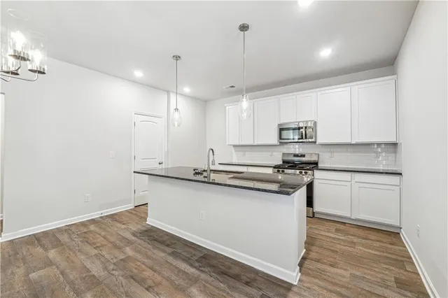 a kitchen with stainless steel appliances granite countertop a sink a stove and white cabinets with wooden floor