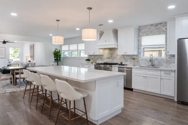 a large kitchen with kitchen island a stove a sink a refrigerator and white cabinets with wooden floor