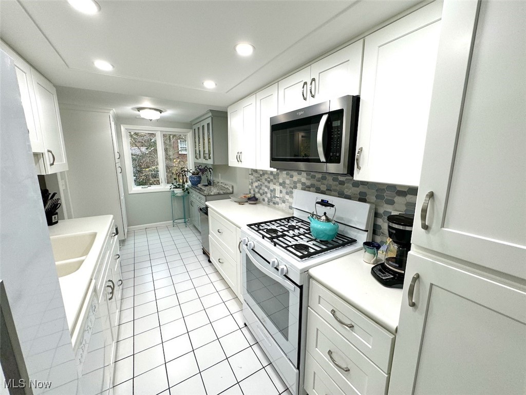 3701 Mayfield Road, Unit 207 Cleveland, OH 44121 - Photo 9 of 30 Kitchen with white cabinets, decorative backsplash, light tile patterned floors, sink, and white gas stove