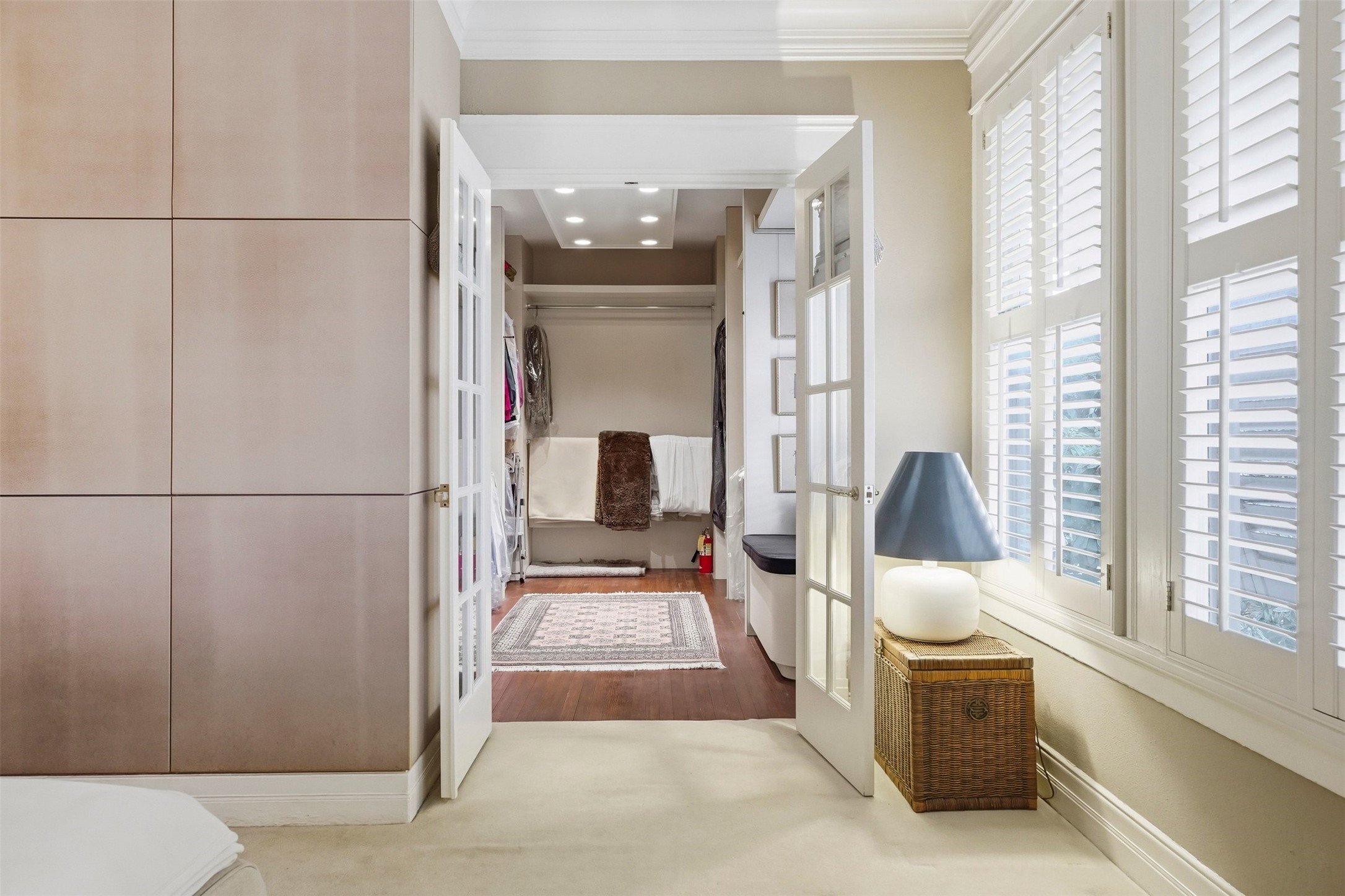 110 Stratford Street Houston, TX 77006 - Photo 18 of 40 This photo features a bright, elegant bedroom with French doors leading to a spacious walk-in closet. It has ample natural light from large windows with shutters and a cozy, warm ambiance.
