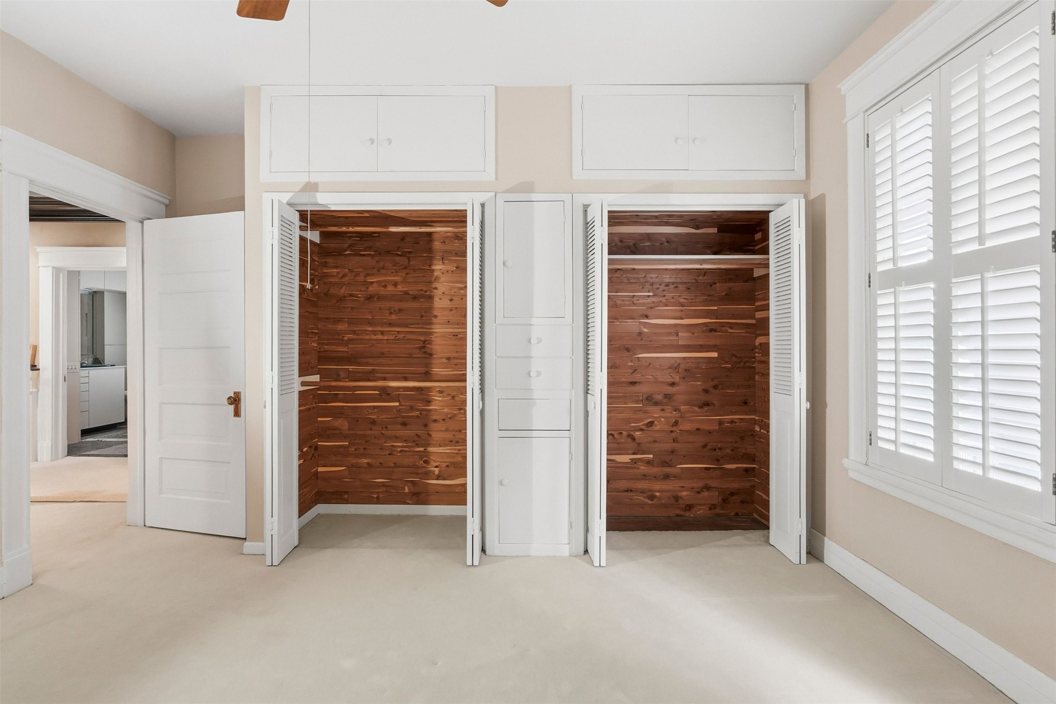 110 Stratford Street Houston, TX 77006 - Photo 23 of 40 Bright room with twin cedar-lined closets, white shutters on the window, and light walls. The space is accented by a ceiling fan and offers ample storage with upper cabinets.