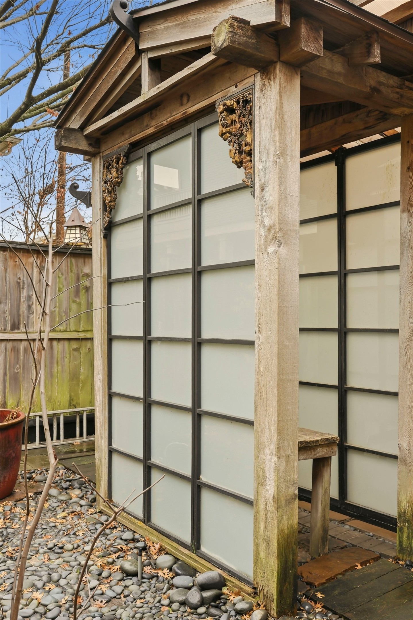 110 Stratford Street Houston, TX 77006 - Photo 33 of 40 This photo showcases a small outdoor structure with a Japanese-inspired design, featuring frosted glass panels in a wooden frame. The area is surrounded by a wooden fence and includes a pebble stone ground, creating a tranquil, private space.