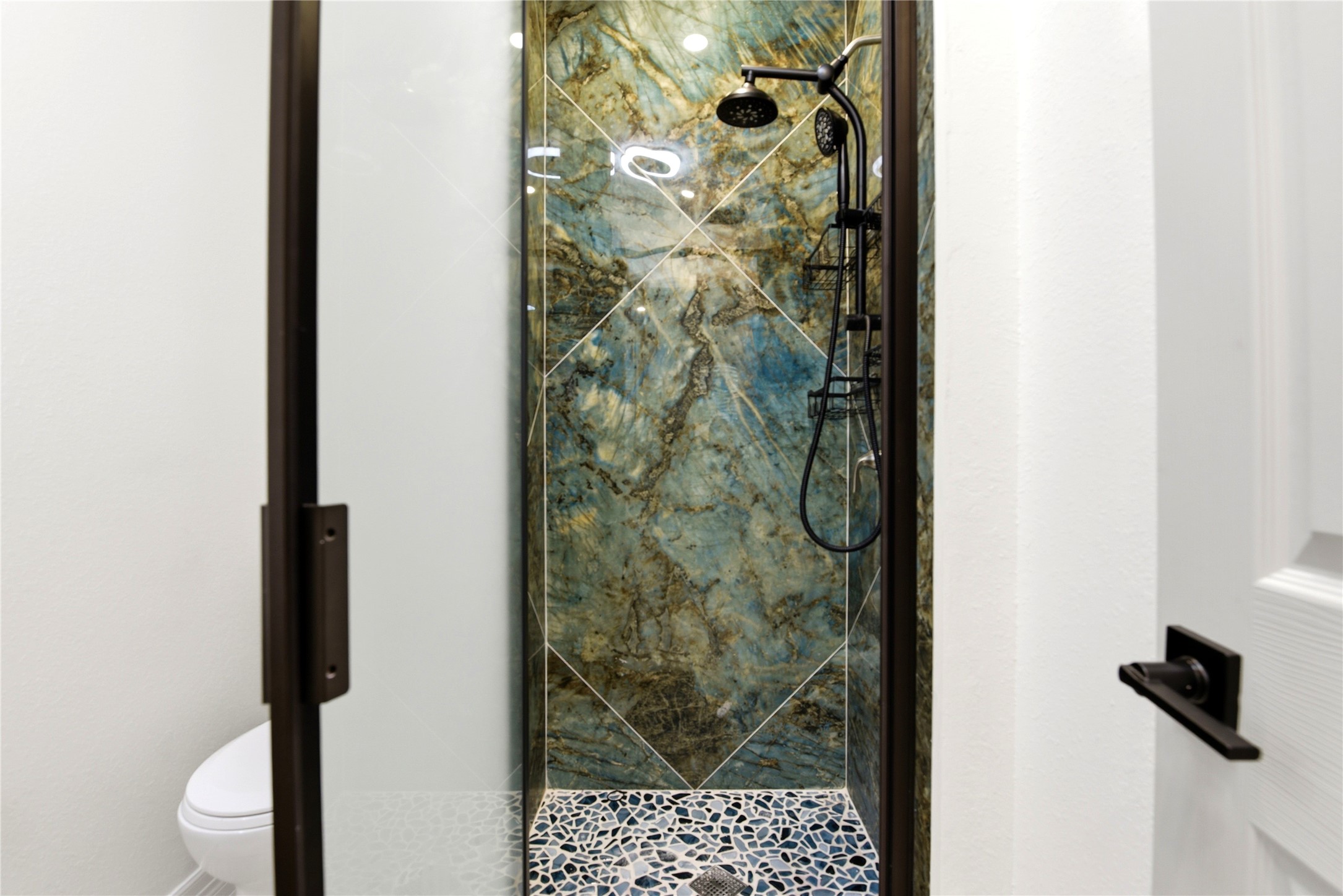 9403 Spaulding Street Houston, TX 77016 - Photo 35 of 50 This photo showcases a modern shower with a striking blue-green stone wall and a sleek black shower fixture. The floor features a stylish mosaic tile design, adding a touch of elegance to the space.
