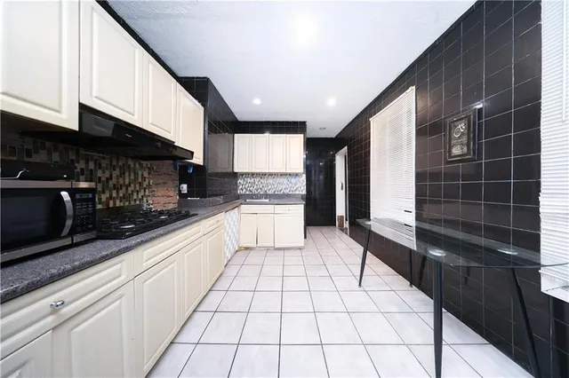 a large white kitchen with granite countertop a stove a microwave a sink and cabinets