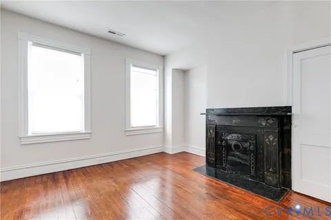 an empty room with wooden floor fireplace and windows