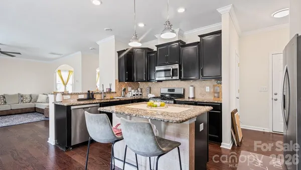 a kitchen with stainless steel appliances granite countertop a stove a sink a microwave a refrigerator and chairs