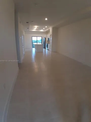 an empty room with large windows and kitchen view