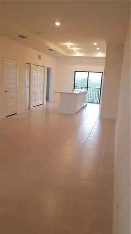 a view of an empty room with wooden floor and kitchen