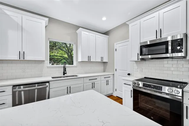 a kitchen with stainless steel appliances granite countertop a sink a window and wooden floor