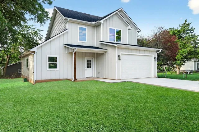a view of a white house in front of a yard with many windows