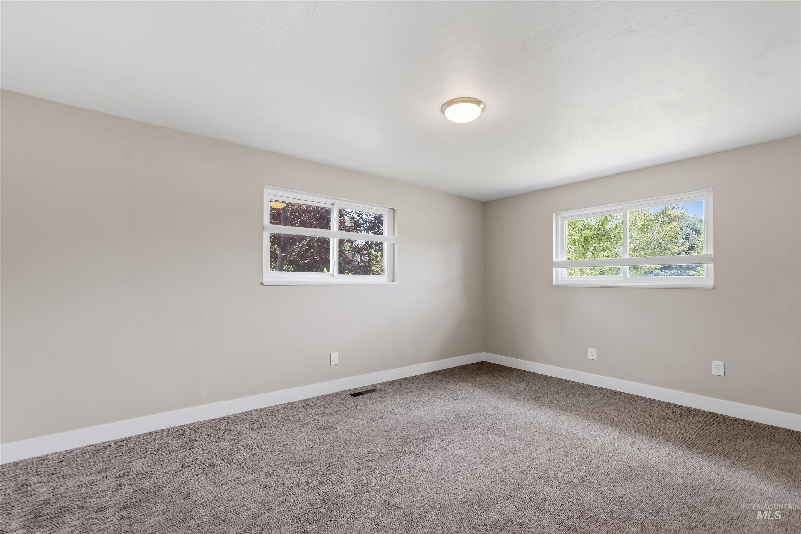 355 East Beacon Light Road Eagle, ID 83616 - Photo 19 of 47 Neutral-toned room featuring a flush-mount ceiling light, two windows, and dark gray carpet flooring