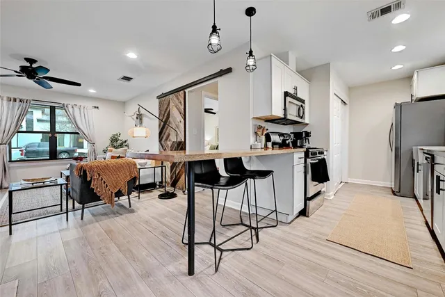 a living room with stainless steel appliances kitchen island granite countertop a table chairs refrigerator and sink