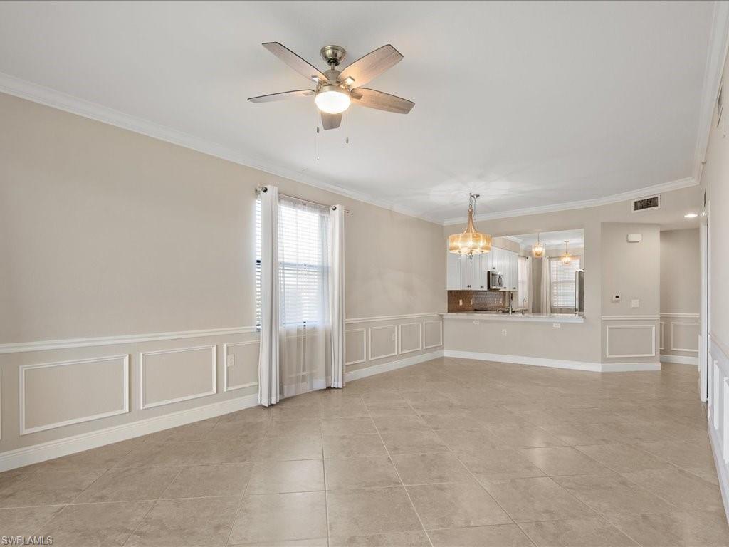 9719 Acqua Court, Unit 218 Naples, FL 34113 - Photo 2 of 23 Unfurnished room with a decorative wall, wainscoting, crown molding, a ceiling fan, and a chandelier