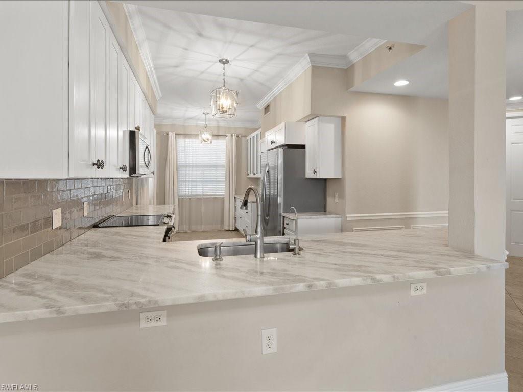 9719 Acqua Court, Unit 218 Naples, FL 34113 - Photo 7 of 23 Kitchen featuring white cabinetry, ornamental molding, a peninsula, light stone countertops, and stainless steel appliances