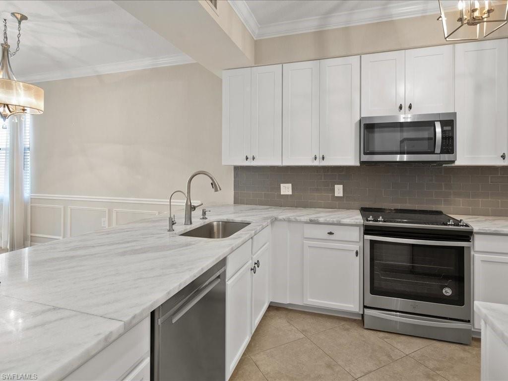 9719 Acqua Court, Unit 218 Naples, FL 34113 - Photo 8 of 23 Kitchen featuring stainless steel appliances, ornamental molding, white cabinets, hanging lights, and light stone counters