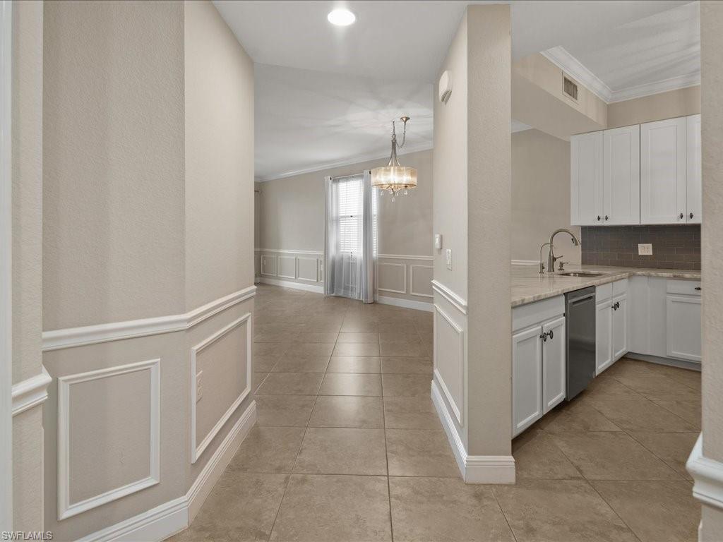 9719 Acqua Court, Unit 218 Naples, FL 34113 - Photo 9 of 23 Kitchen with a decorative wall, wainscoting, white cabinetry, crown molding, and a chandelier