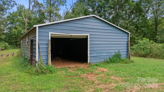 a view of barn house with a small yard plants and large trees
