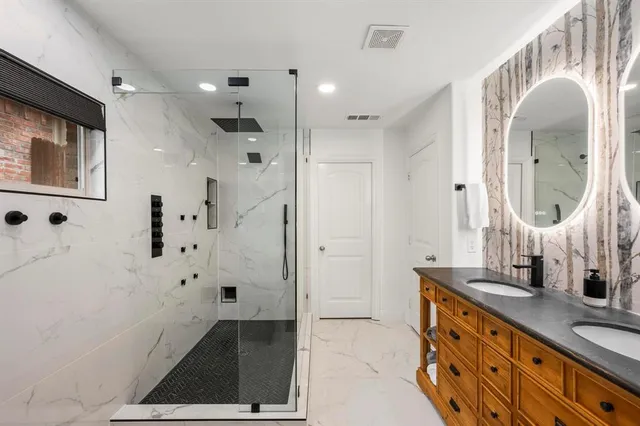 a bathroom with double vanity sink a mirror a glass door a shower and vanity