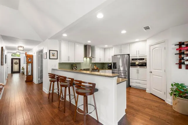 a kitchen with stainless steel appliances granite countertop a refrigerator a stove top oven a sink a dining table and chairs with wooden floor