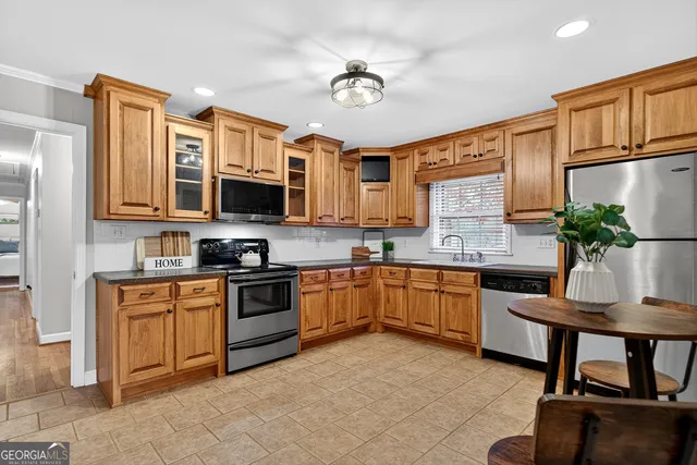 a kitchen with stainless steel appliances granite countertop a stove top oven a sink dishwasher a dining table and chairs with wooden cabinets