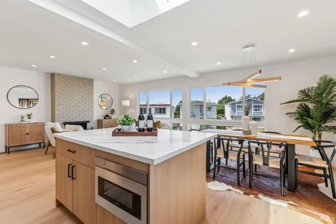 a living room with stainless steel appliances kitchen island granite countertop a refrigerator a stove and a sink with wooden floor
