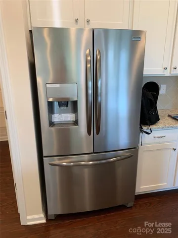 a view of a refrigerator in kitchen and an empty room with wooden floor