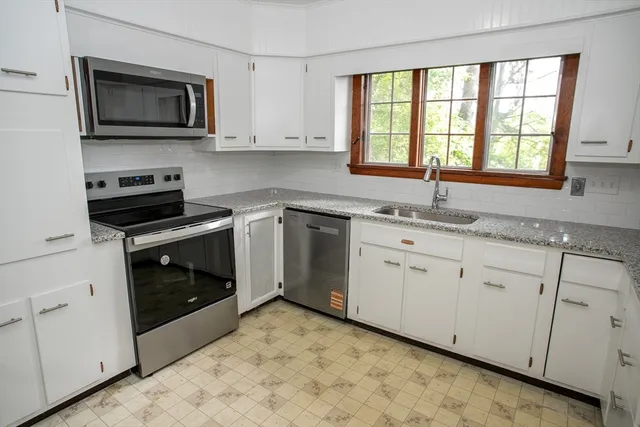 a kitchen with granite countertop white cabinets appliances and a window