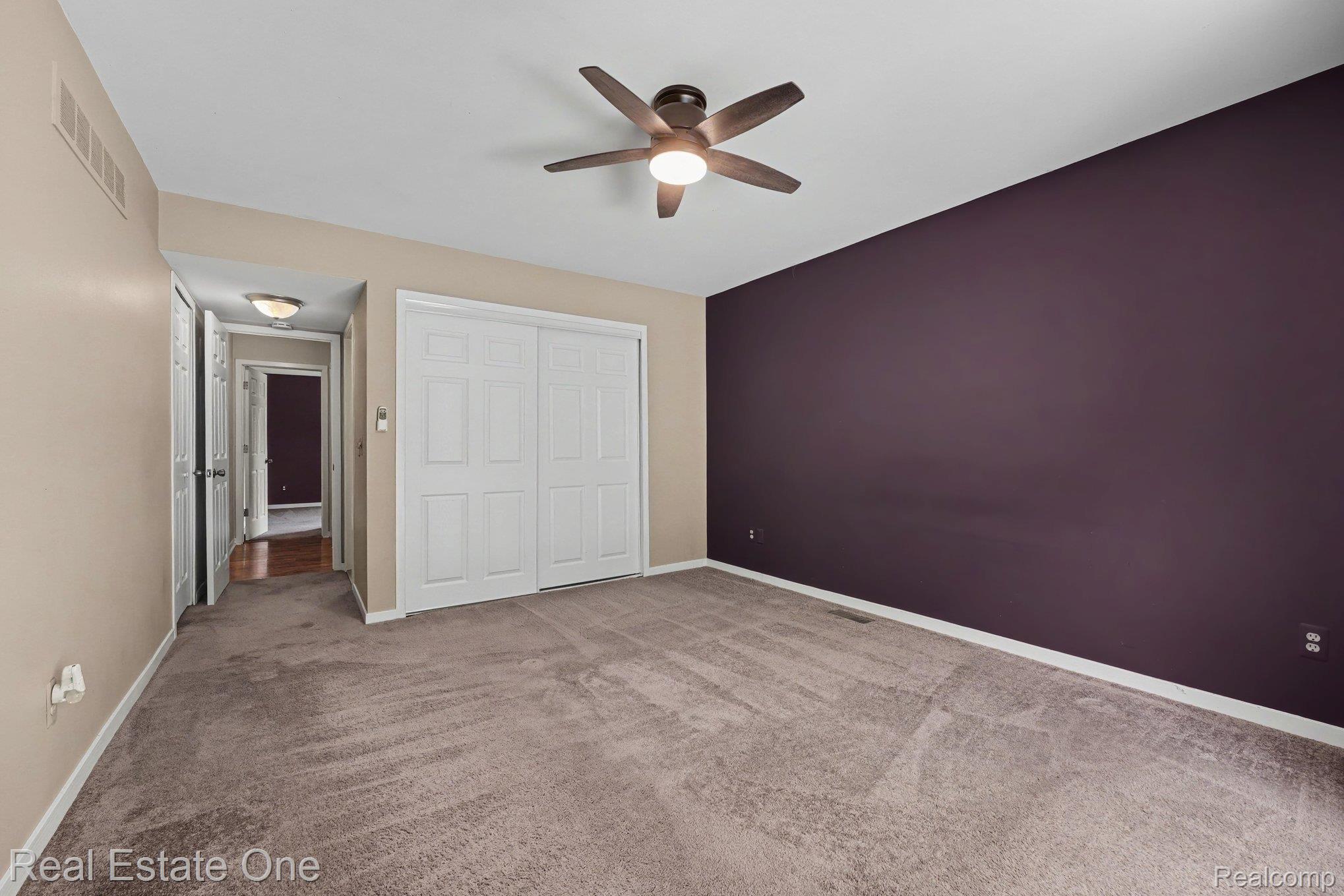 701 Charing Court Rochester, MI 48307 - Photo 12 of 29 Spacious carpeted room featuring a ceiling fan with integrated lighting, a dedicated accent wall, and bi-fold closet doors
