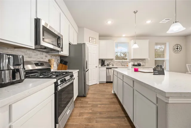 a kitchen with stainless steel appliances granite countertop a stove top oven a refrigerator a sink and dishwasher with white cabinets