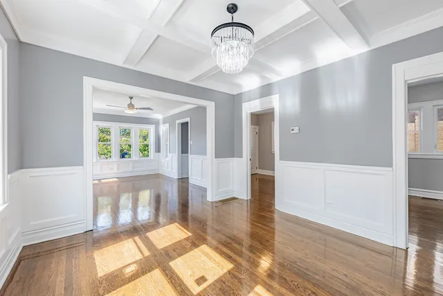 a view of an empty room and kitchen with wooden floor