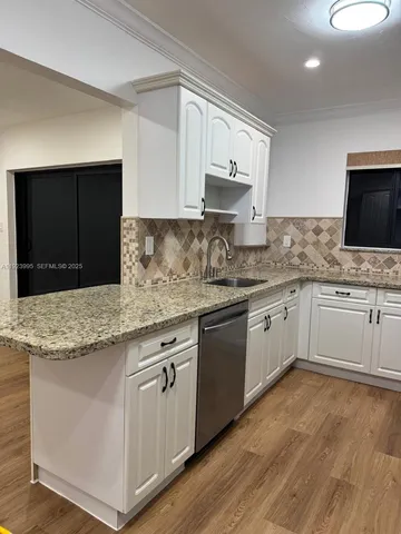 a white kitchen with granite countertop stainless steel appliances and sink