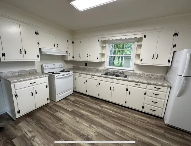 a kitchen with granite countertop white cabinets white appliances a sink and a window