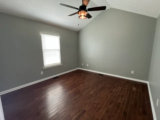 an empty room with wooden floor ceiling fan and windows