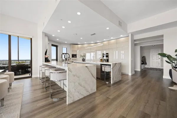 a living room with stainless steel appliances furniture wooden floor and a kitchen view