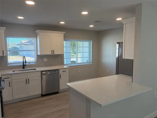 a kitchen with granite countertop white cabinets a sink dishwasher and a stove with wooden floor