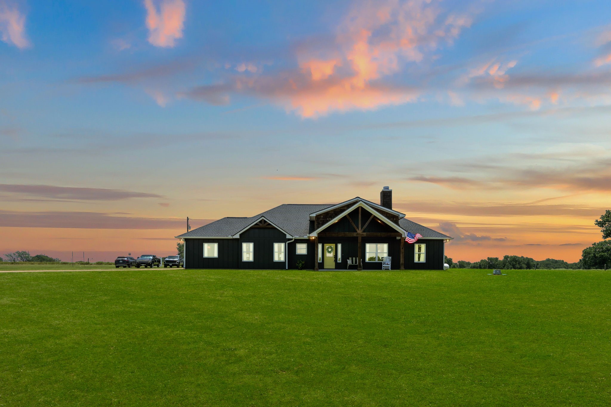 1655 Old Cuero Road Yoakum, TX 77995 - Photo 2 of 24 This stunning twilight exterior showcases the home's striking modern farmhouse design against a breathtaking Texas sunset. Bold black board-and-batten siding, warm timber accents, and a welcoming covered front porch create exceptional curb appeal, while expansive manicured lawns and wide-open acreage provide a true sense of space and privacy.