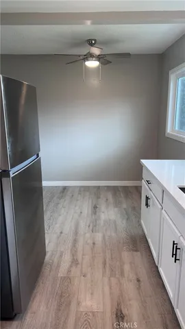 a view of a refrigerator in kitchen and an empty room with wooden floor