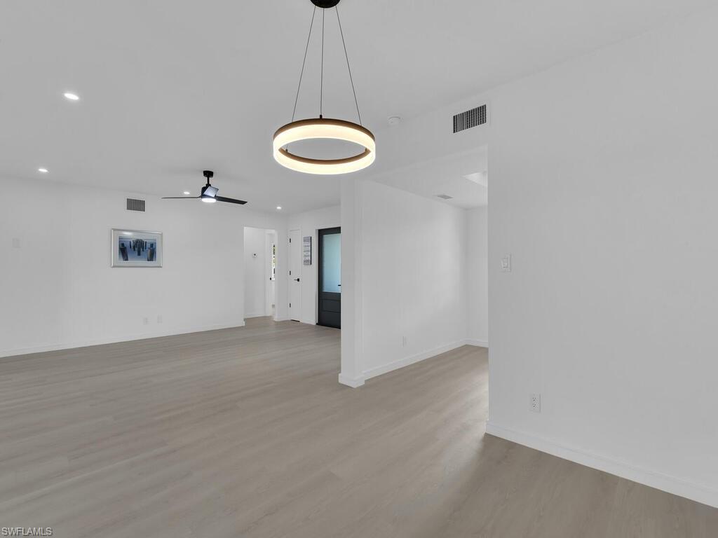 4941 Aztec Circle Naples, FL 34112 - Photo 15 of 36 an empty room with a chandelier fan and wooden floor
