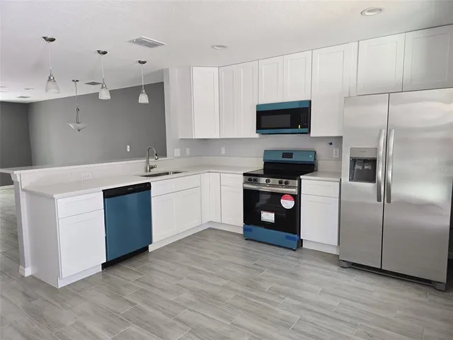 a kitchen with stainless steel appliances white cabinets a sink a stove a refrigerator and a microwave