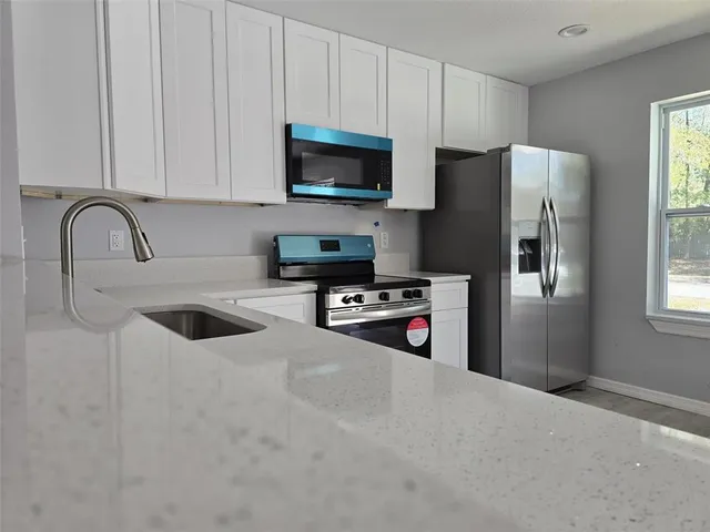 a kitchen with stainless steel appliances granite countertop a refrigerator a stove a sink and a white cabinets