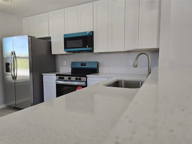 a kitchen with stainless steel appliances granite countertop a refrigerator a stove a sink and a white cabinets