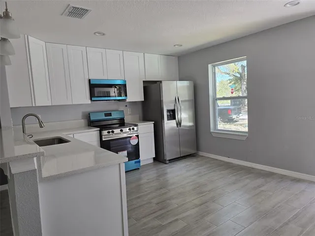 a kitchen with stainless steel appliances a microwave a sink a stove a refrigerator cabinets and a window