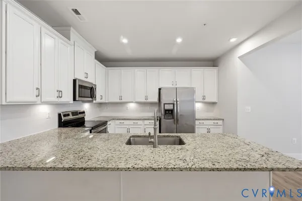 a kitchen with stainless steel appliances granite countertop a sink a stove and a refrigerator with white cabinets