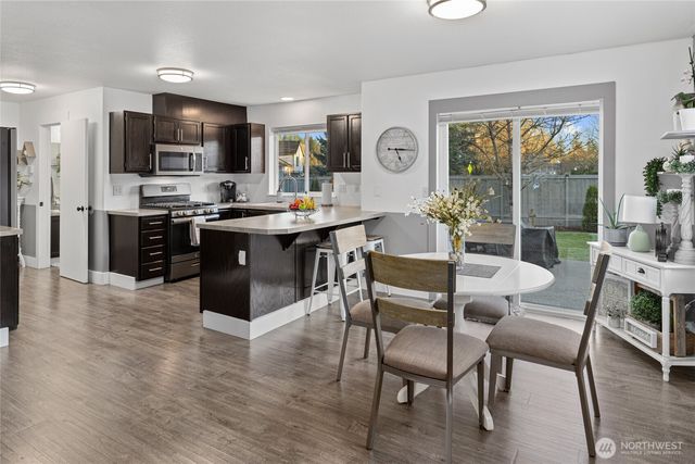 a open kitchen with stainless steel appliances granite countertop a stove top oven a sink dishwasher a dining table and chairs with wooden floor